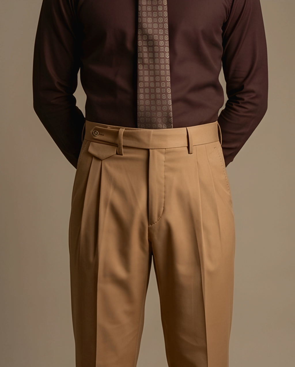 Man wearing a brown shirt with a patterned tie and beige pants against a neutral background